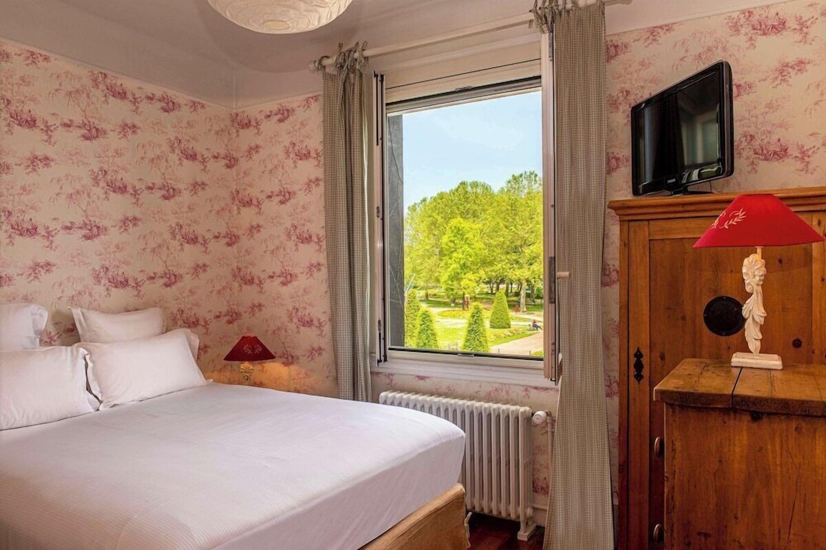Ein Schlafzimmer mit einem Bett, einem Fenster mit Blick auf Bäume, einem Holzschrank und einem Fernseher.