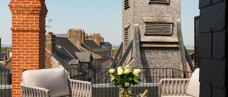 Une terrasse sur le toit avec deux fauteuils en osier, une table ornée d’un vase de fleurs, un seau à champagne et une vue sur le paysage urbain.