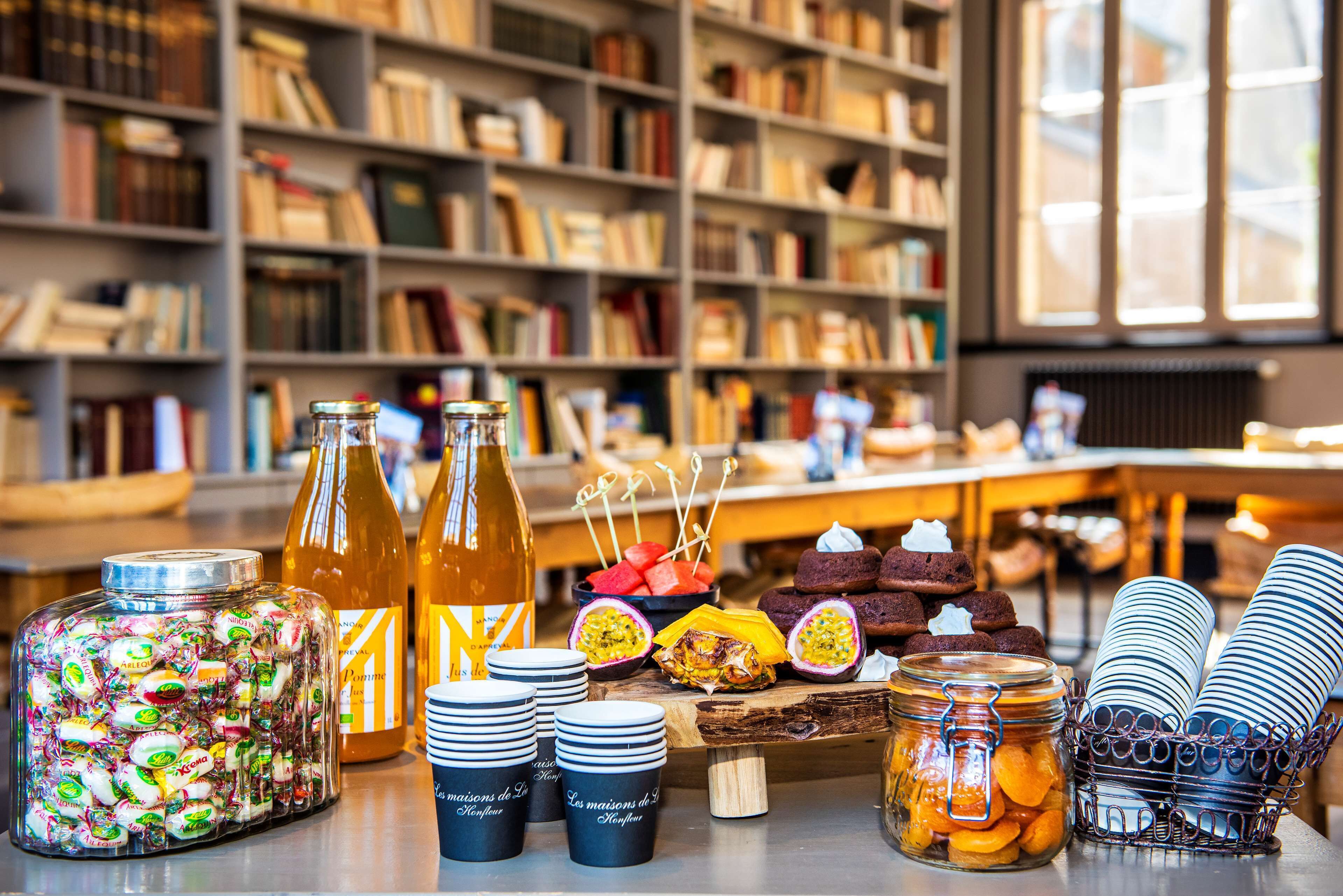 A table with jars of sweets, bottles, and plates in a room with bookshelves.