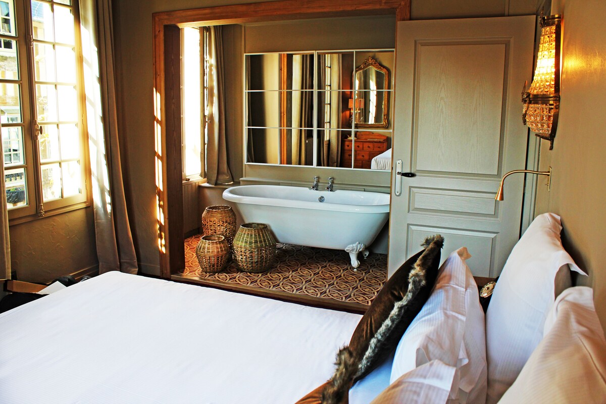 Ein Hotelzimmer mit einem großen Bett, einer Badewanne, einem Spiegel und einem Fenster mit Vorhängen.