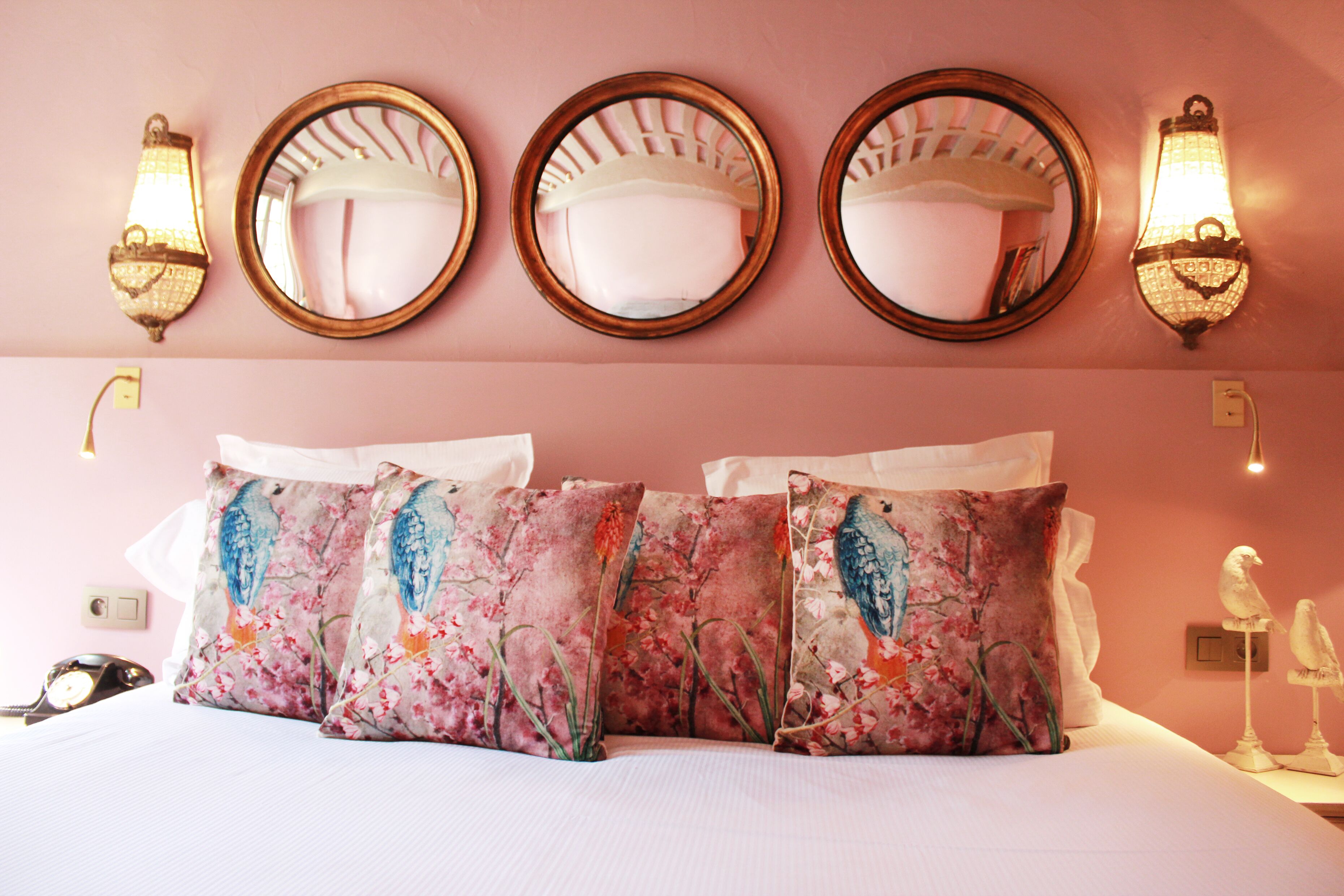 Une chambre d’hôtel avec un lit, des coussins à motifs floraux, des miroirs fixés au mur et des appliques murales.