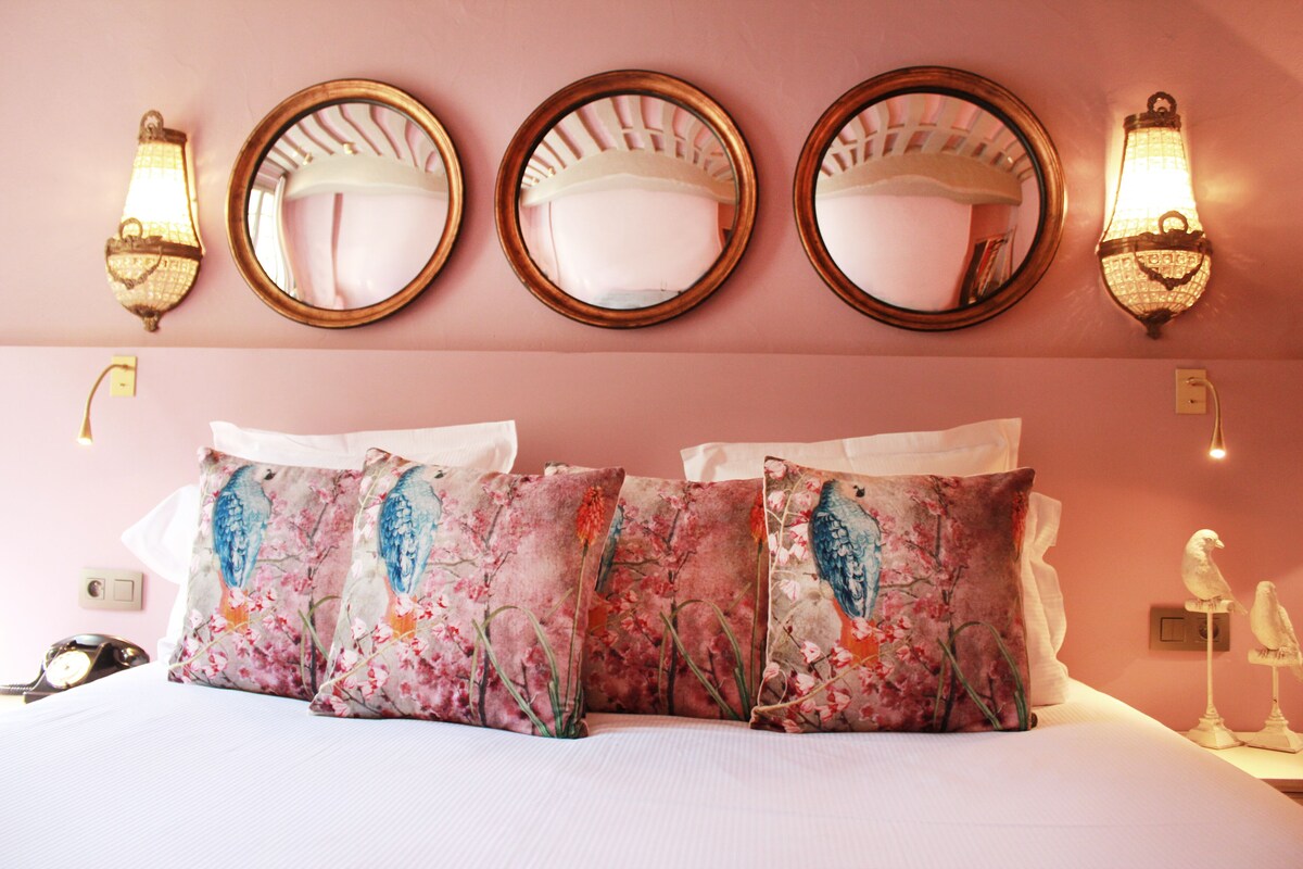 Ein Hotelzimmer mit einem Bett, blumigen Kissen, Wandspiegeln und Wandleuchten.