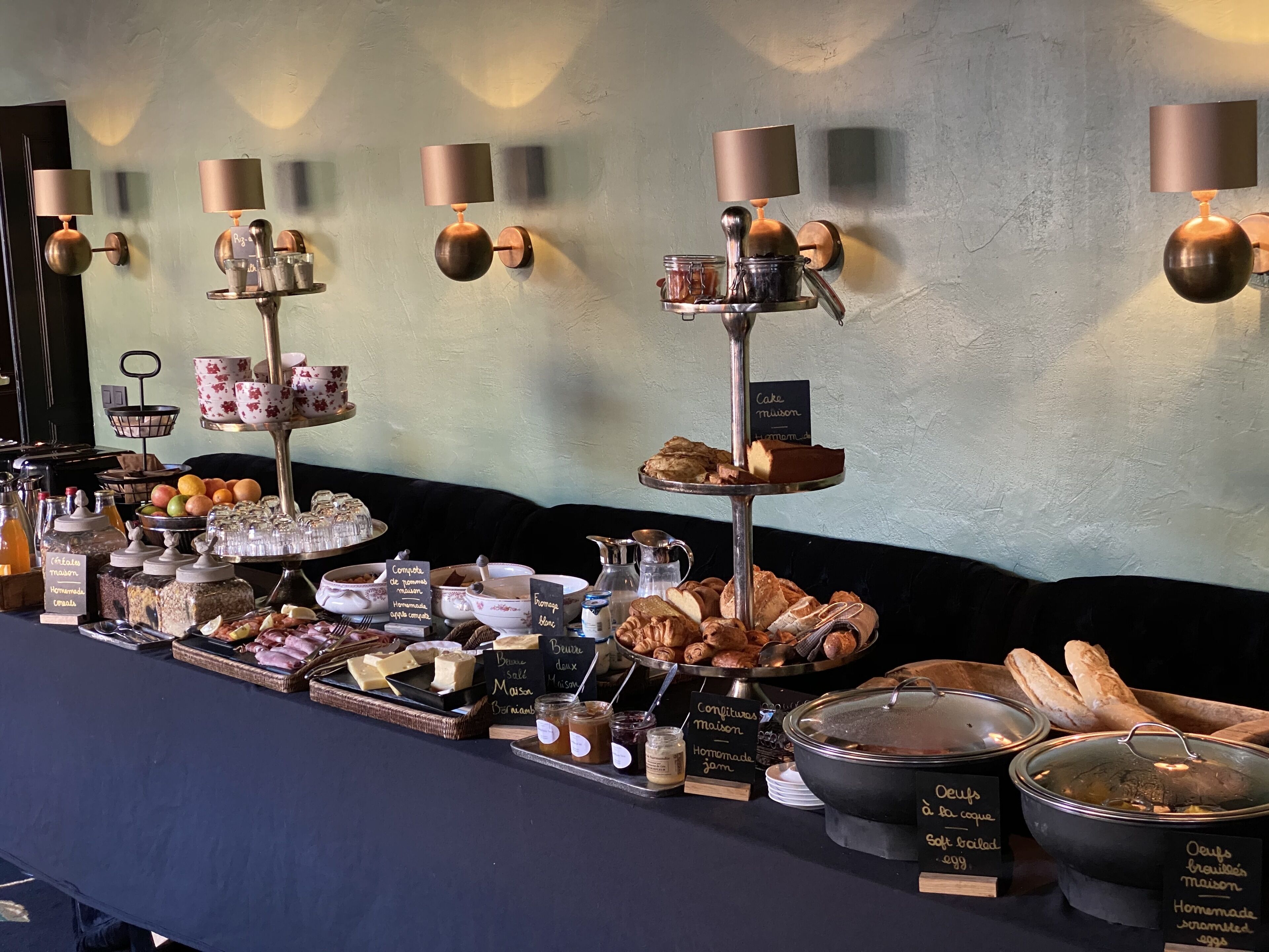 A breakfast buffet with various food items and condiments, including pastries, breads, and spreads, displayed on a long table with labels in French.