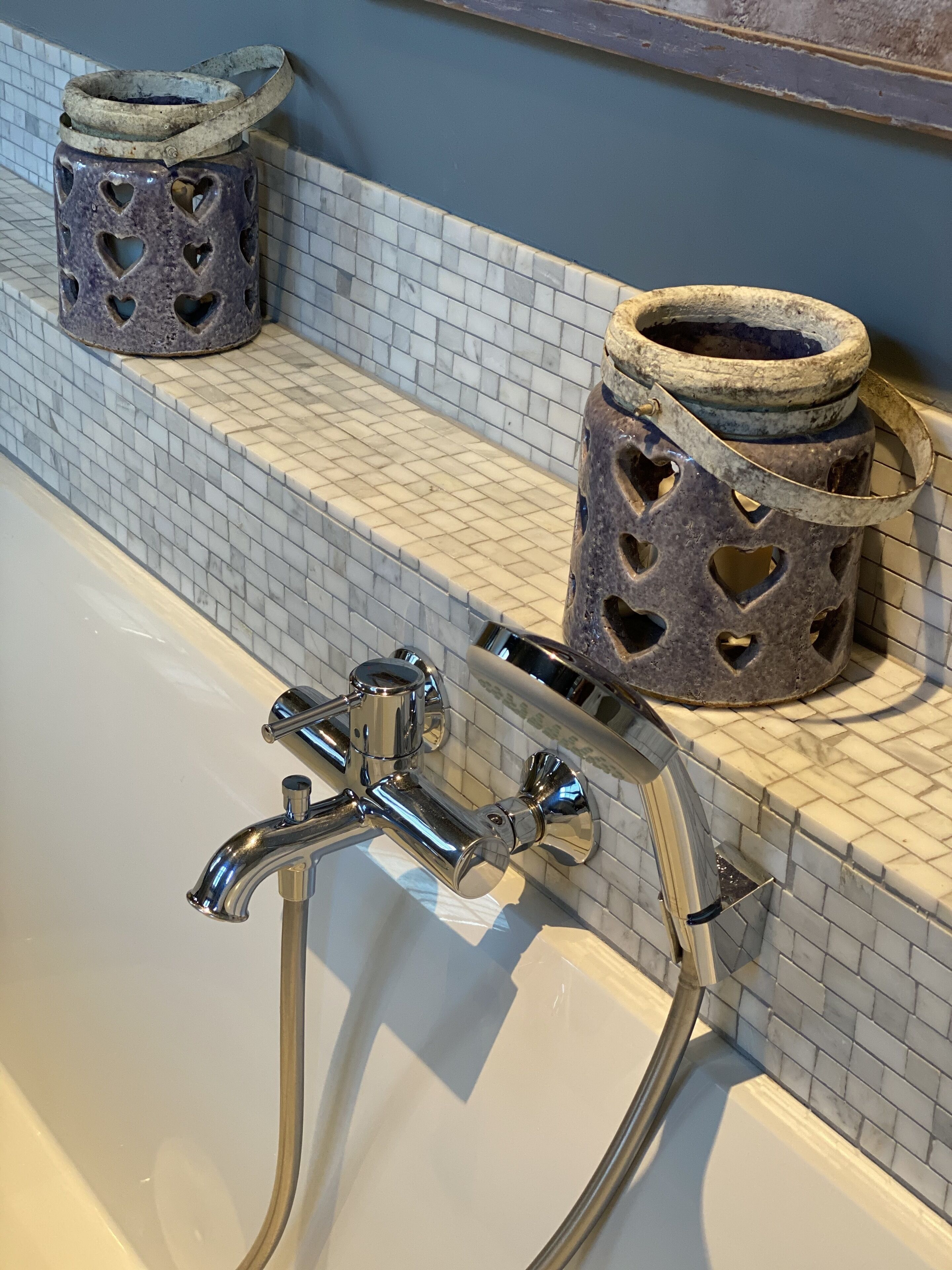 Un baño con bañera, grifo de cromo y dos portavelas con forma de corazón sobre un repisa con azulejos.