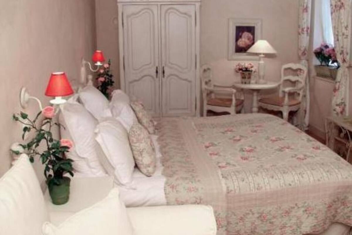 Un dormitorio con cama, una silla, una mesa, un armario y una lámpara.