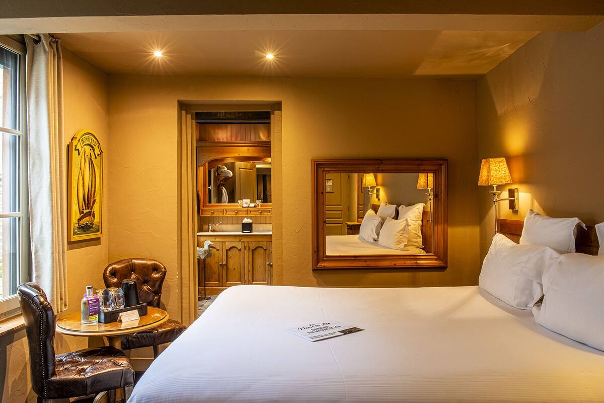 Habitación de hotel con una cama grande, una silla, un escritorio con artículos de aseo, un espejo y una ventana con cortinas.