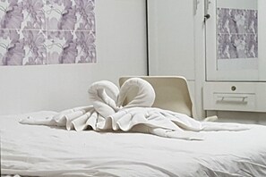 A bed with a white blanket and pillows, a white cabinet with a drawer, and a wall with a floral pattern. - Airportlink Lardkrabang Mansion (Bangkok)