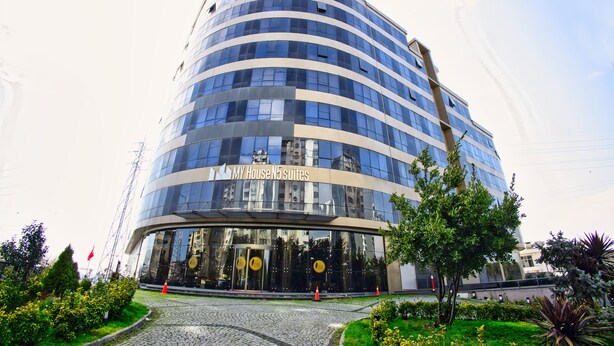 Un hotel moderno con fachada curva, amplios ventanales de vidrio y un letrero que dice "MY House N5 suites".
