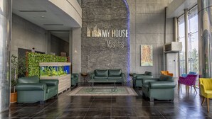Un moderno vestíbulo con mostrador de recepción, sofás verdes y una pared grande con letrero 'MY HOUSE N5 suites'.