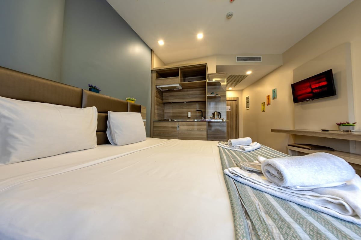 A hotel room with a large bed, a small kitchenette, a TV, and a bathroom.