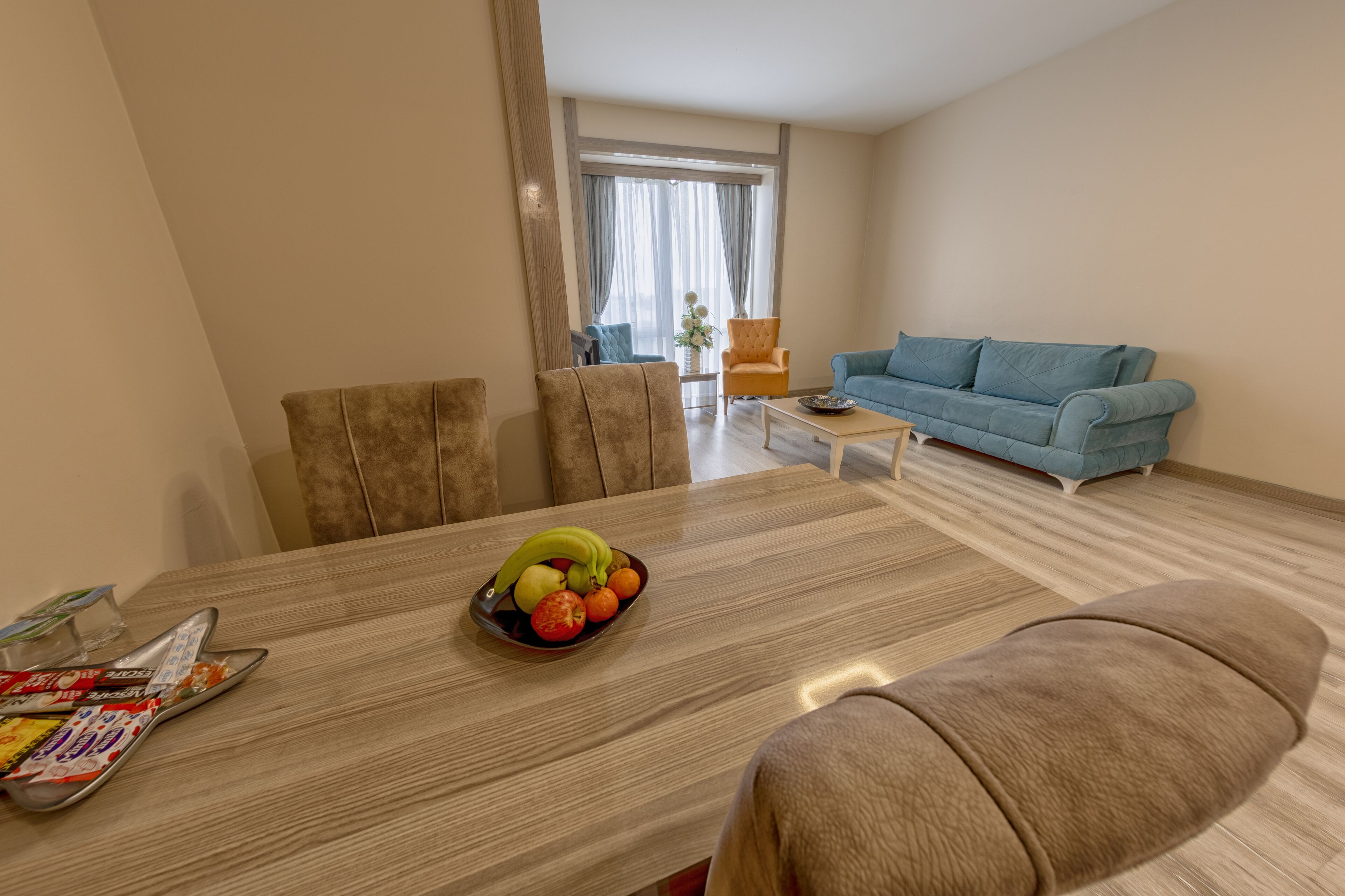 A modern living room with a blue sofa, a dining table with fruit, and a coffee table.