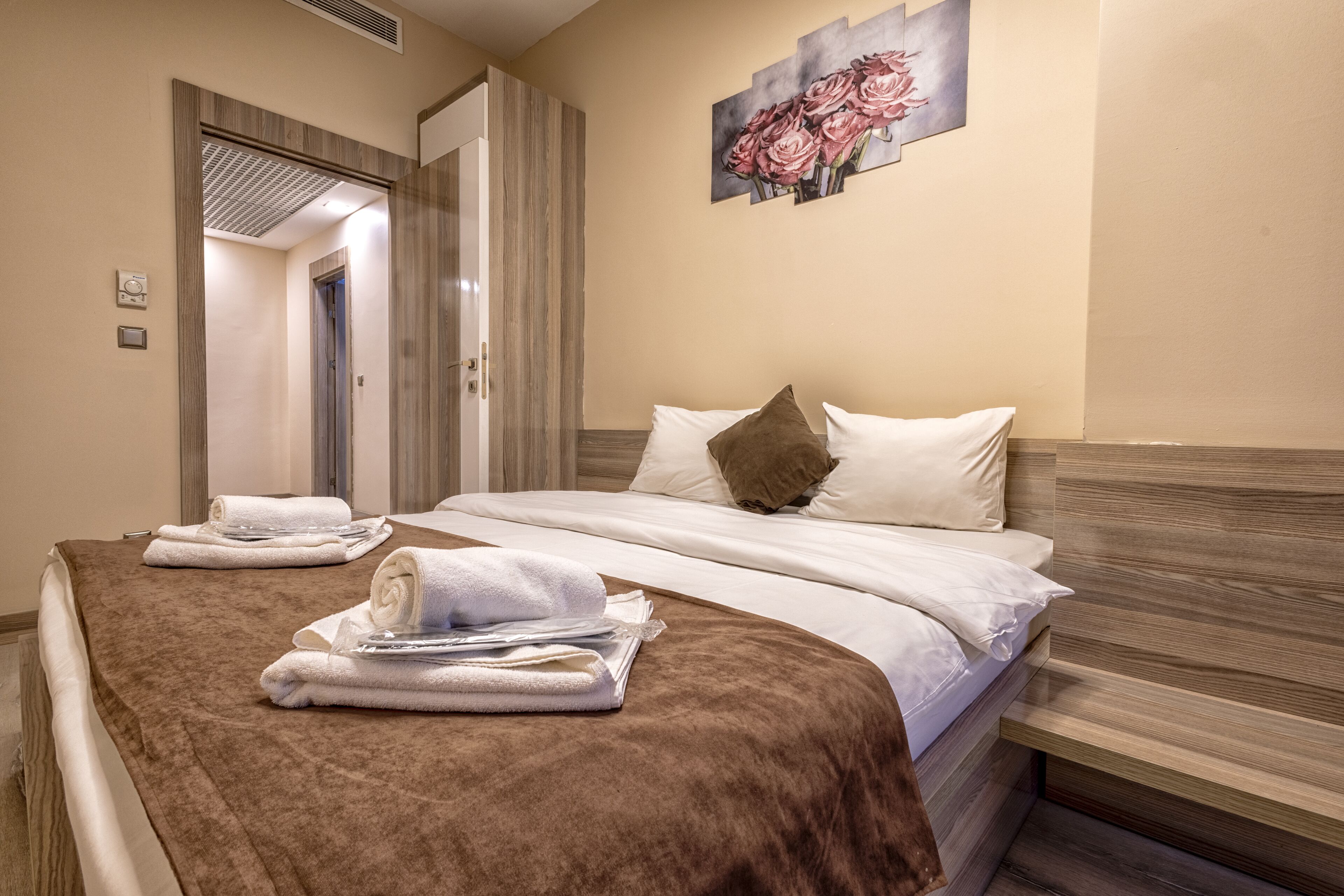 A hotel room with a bed, two towels, a painting, and a door leading to another room.