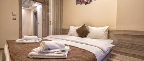 A hotel room with a bed, two towels, a painting, and a door leading to another room.