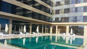 Una piscina con sillas de descanso y sombrillas, rodeada por un edificio moderno con grandes ventanales.