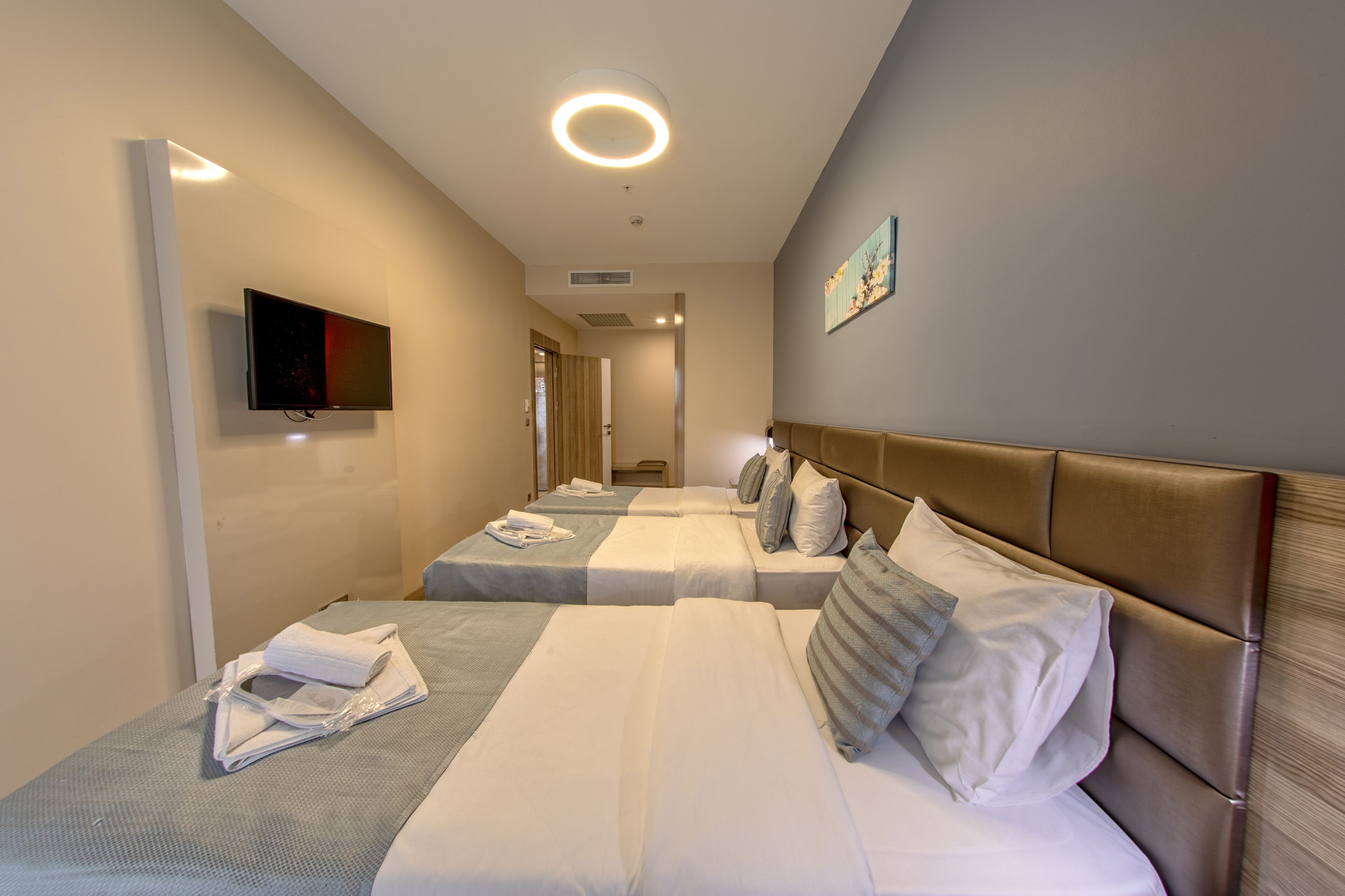 A hotel room with three beds, a flat-screen TV, and a painting on the wall.
