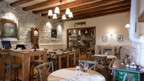 A rustic restaurant interior with exposed wooden beams, stone walls, and traditional decor. Tables are set with plates and cutlery, and a vintage stove is visible. - L'hôtellerie de La toile à beurre (Ancenis-Saint-Géréon)