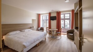 A hotel room with a large bed, a desk with a chair, a round table with chairs, a television, and a window with curtains. - L'hôtellerie de La toile à beurre (Ancenis-Saint-Géréon)