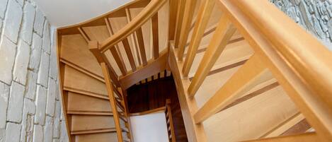 A spiral staircase with wooden railings and a stone wall on one side.