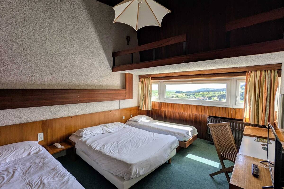 A hotel room with two beds, a desk, and a view of the countryside.