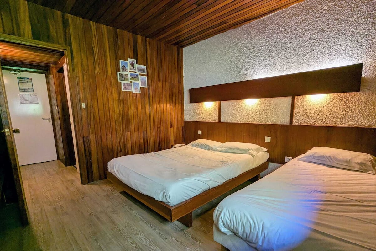 A room with two beds, wooden walls, and a textured ceiling.