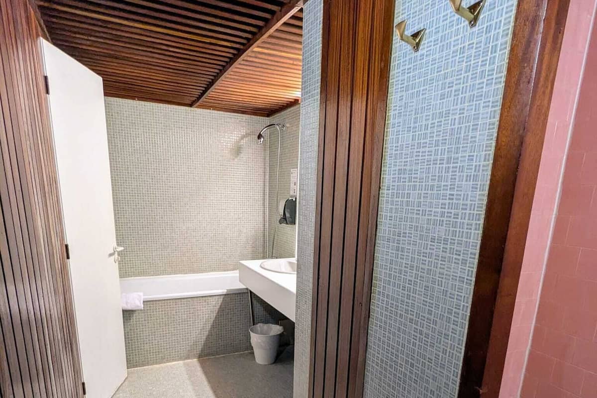 A narrow bathroom with a shower, a sink, and a toilet.