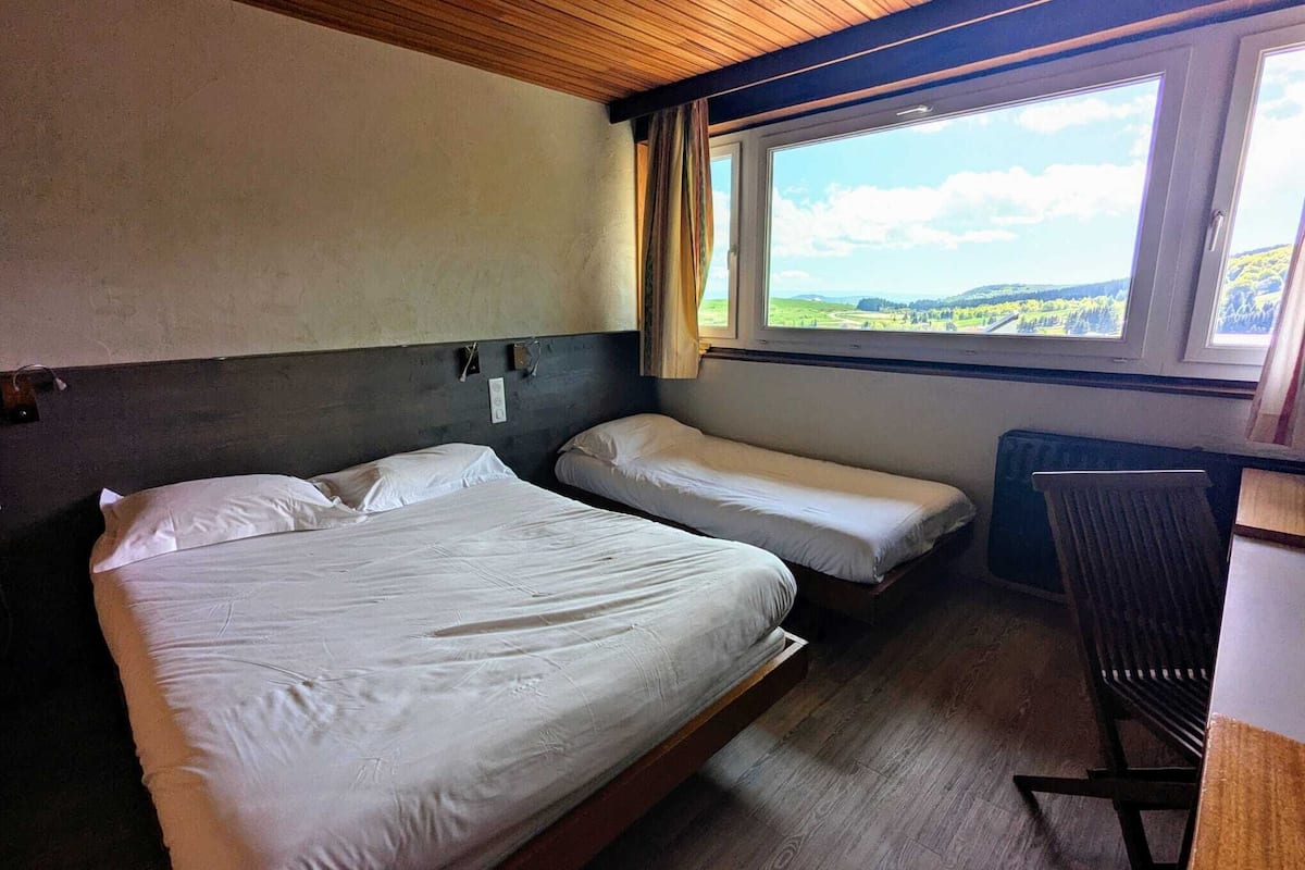 A room with two beds, a window with a view of the countryside, and a radiator.