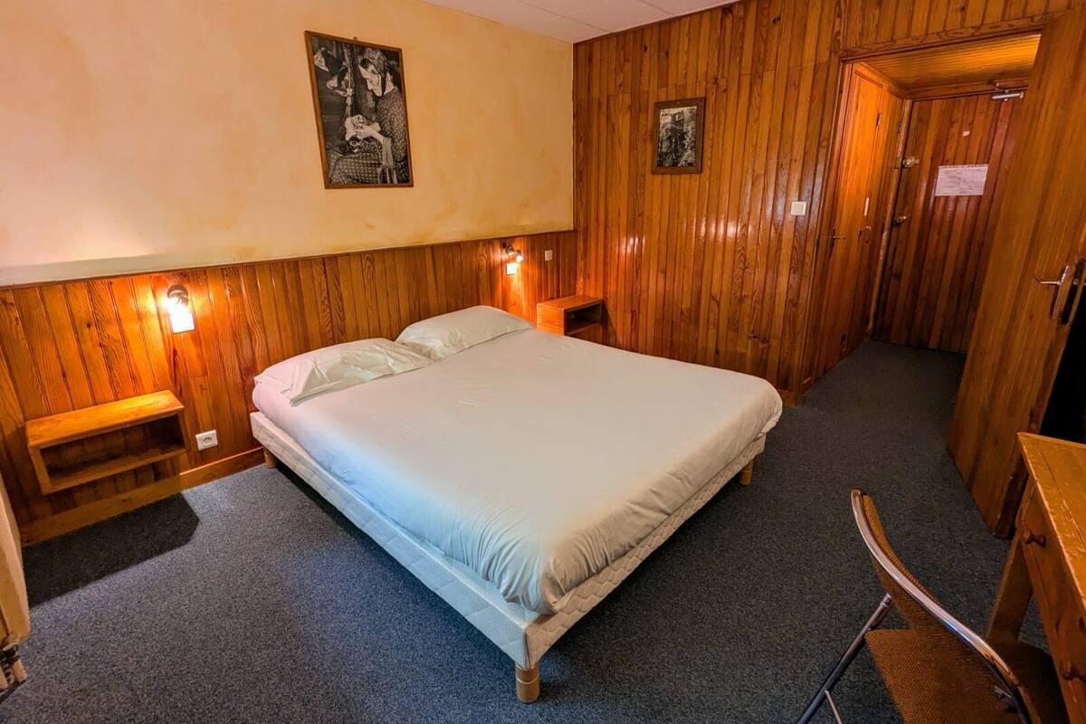 A single-bed room with wooden paneling, a headboard, two bedside tables with lamps, and a small wooden bench.