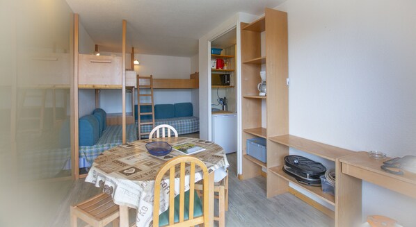 A compact room with bunk beds, a small kitchenette, and a dining area with a table and chairs.