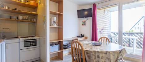 A compact kitchen with a stove, oven, and shelves with dishes. There's a dining table with chairs and a TV mounted on the wall.