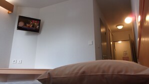 Ett sovrum med en säng, en väggmonterad TV och en dörr som leder till ett annat rum.