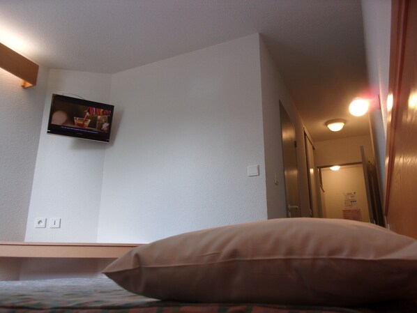 A bedroom with a bed, a wall-mounted TV, and a door leading to another room.