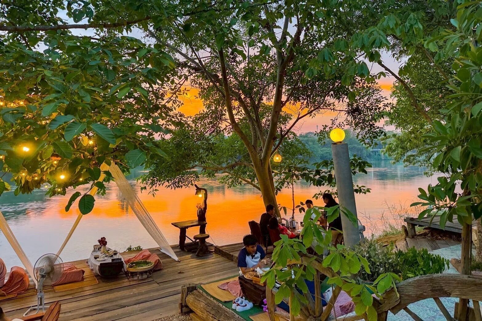 A wooden deck with tables and chairs, overlooking a calm body of water during sunset.