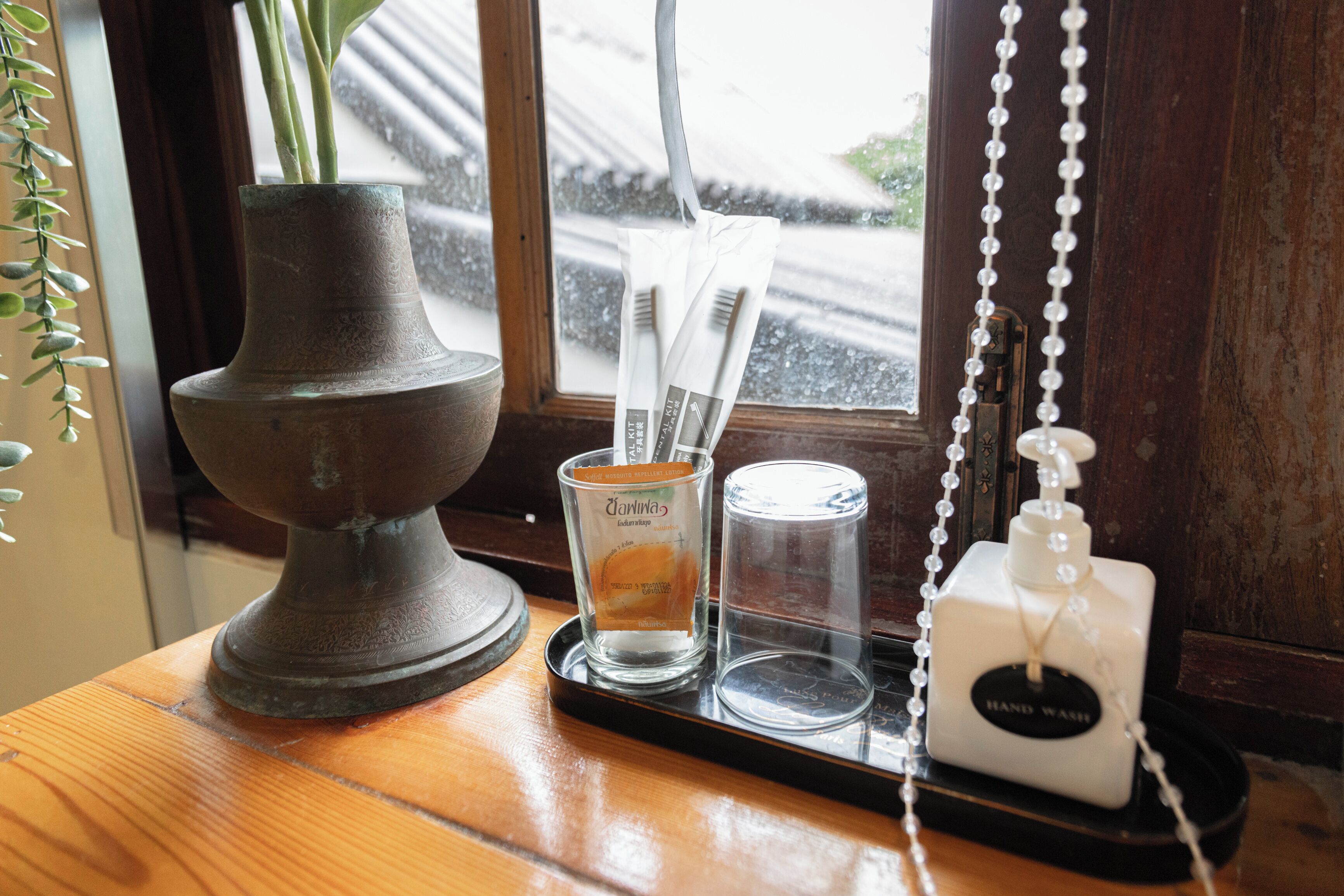 A wooden table with a vase, a candle, a glass, and a hand sanitizer dispenser.
