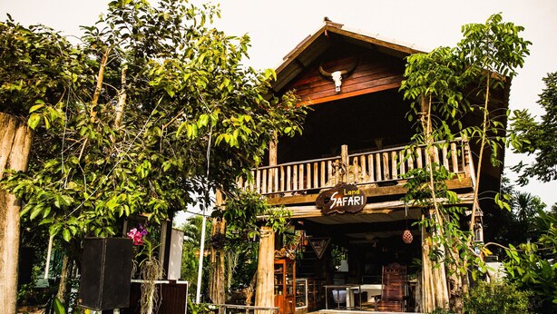 A rustic building with a wooden balcony, surrounded by lush greenery and a sign that reads "Land Safari." - The Antique Riverside (Ban Pong)