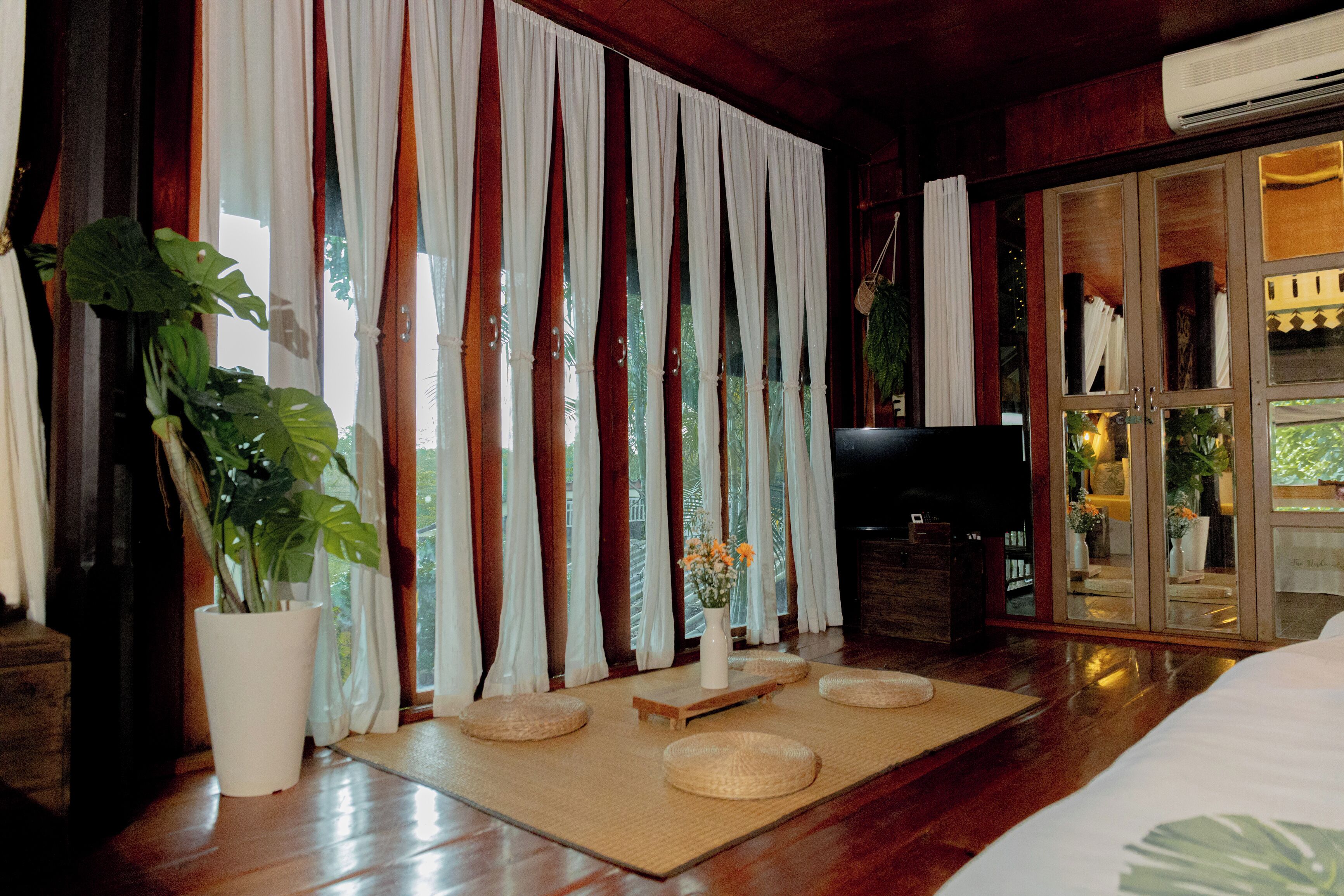 Una habitación con un ventanal grande, una planta en maceta, un banco de madera y un televisor.