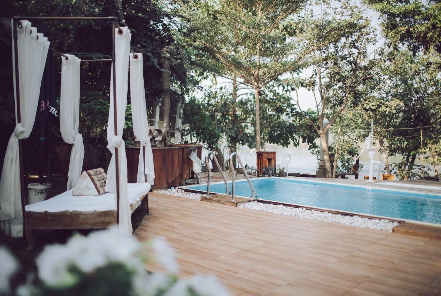 A wooden deck with a pool, a canopy bed, and trees in the background.