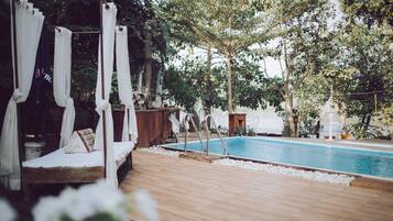 A wooden deck with a pool, a canopy bed, and trees in the background.