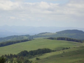 Una vista panorámica de un valle verde con colinas ondulantes y montañas lejanas.