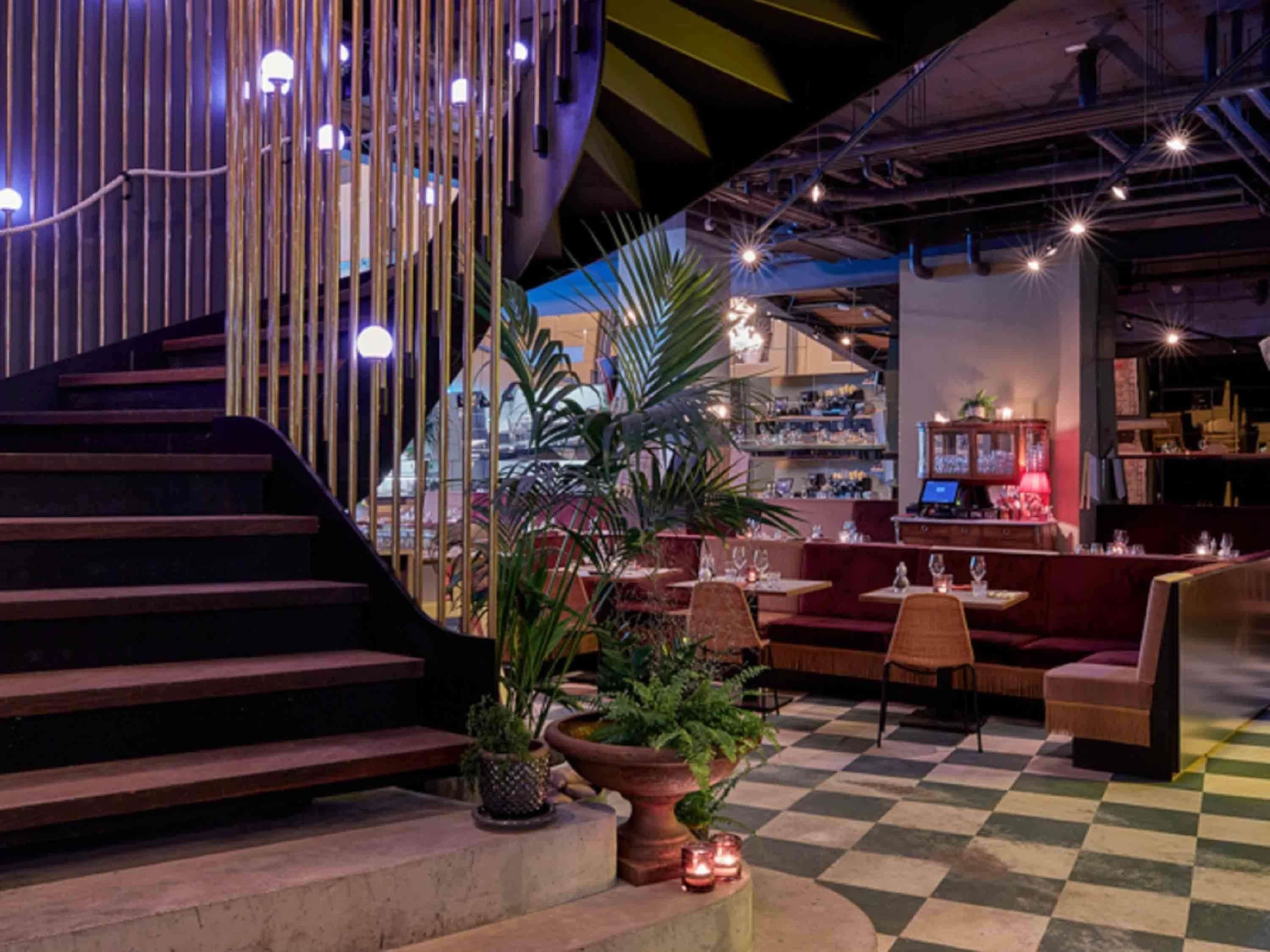 A restaurant with a checkered floor, wooden staircase, and potted plants.