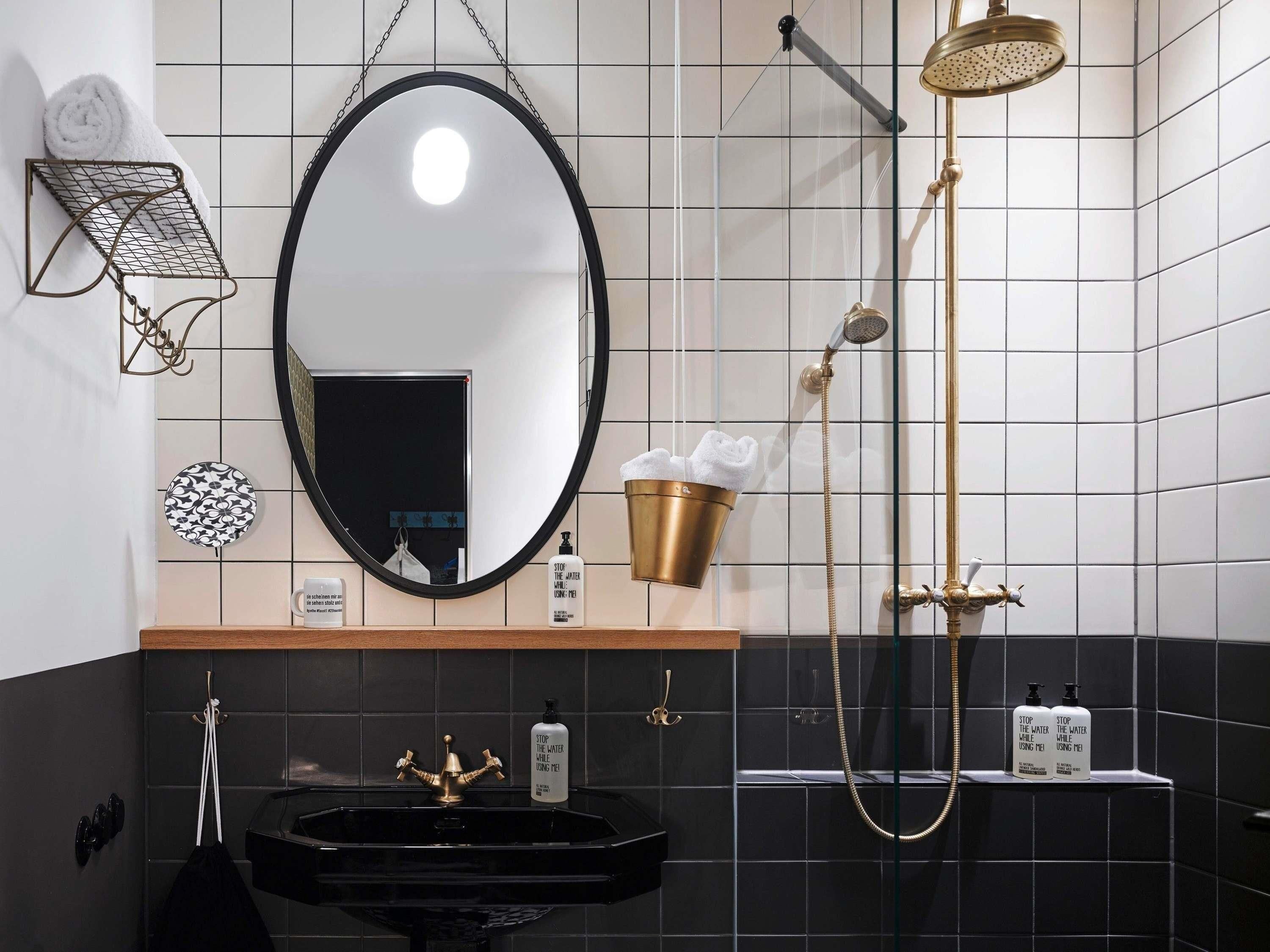 A bathroom with a black sink, a gold showerhead, and a mirror with a black frame.