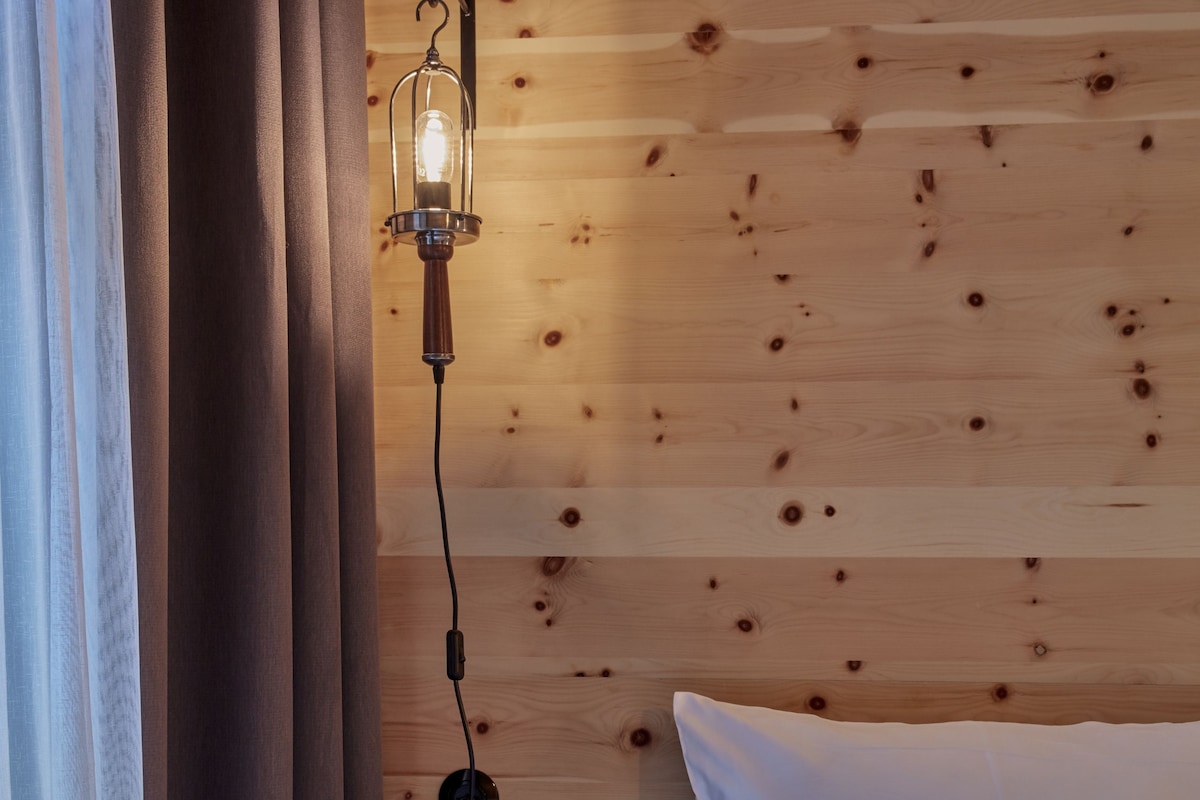 Ein Zimmer in einer Holzhütte mit einem Bett, einem Nachttisch, einer Lampe und einem an der Wand befestigten Regal.