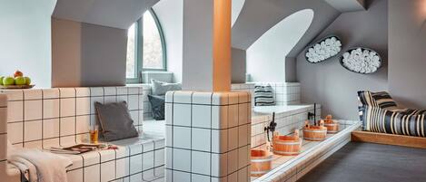 A modern bathroom with a tiled bench, a bathtub, and wooden buckets.