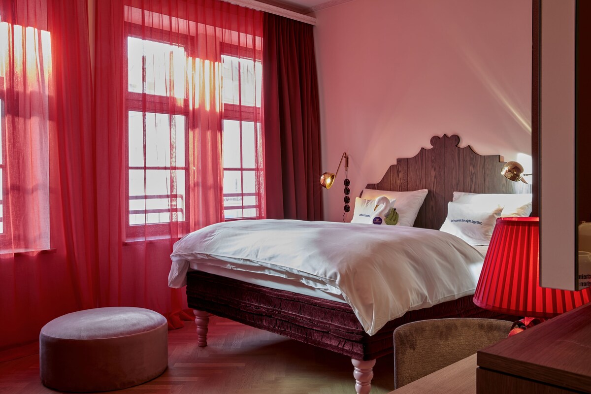 Ein Schlafzimmer mit einem großen Bett, roten Vorhängen, einem Holz-Kopfteil und einer Nachttischlampe.