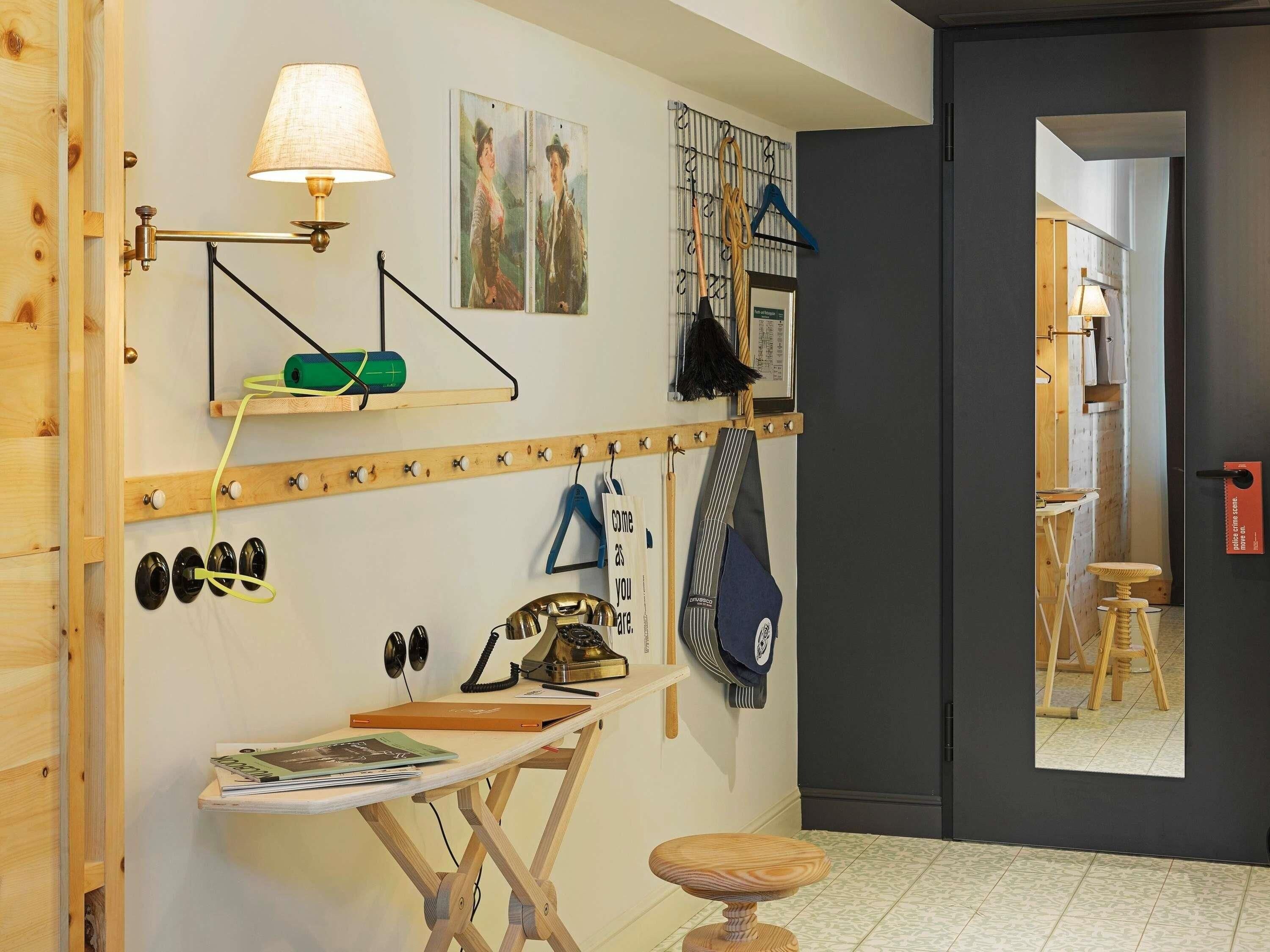 A room with a wooden desk, a lamp, a mirror, and a coat rack.