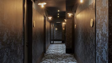 A hallway with patterned carpet, wall sconces, and doors.