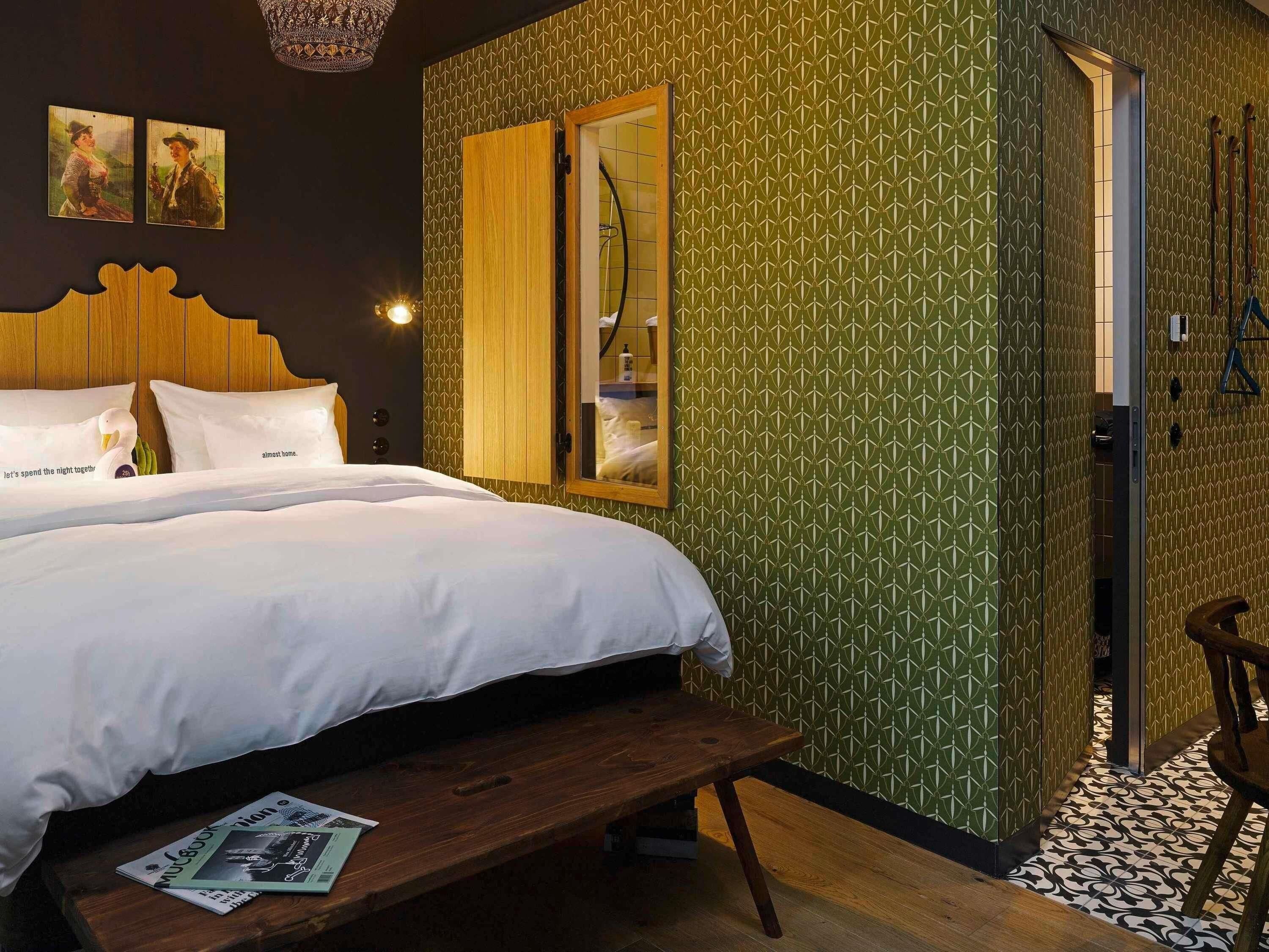 A bedroom with a bed, a wooden bench, a mirror, and a shower area.