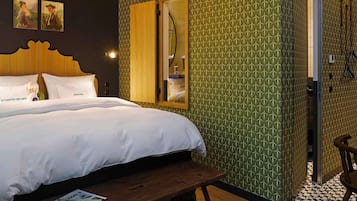 A bedroom with a bed, a wooden bench, a mirror, and a shower area.