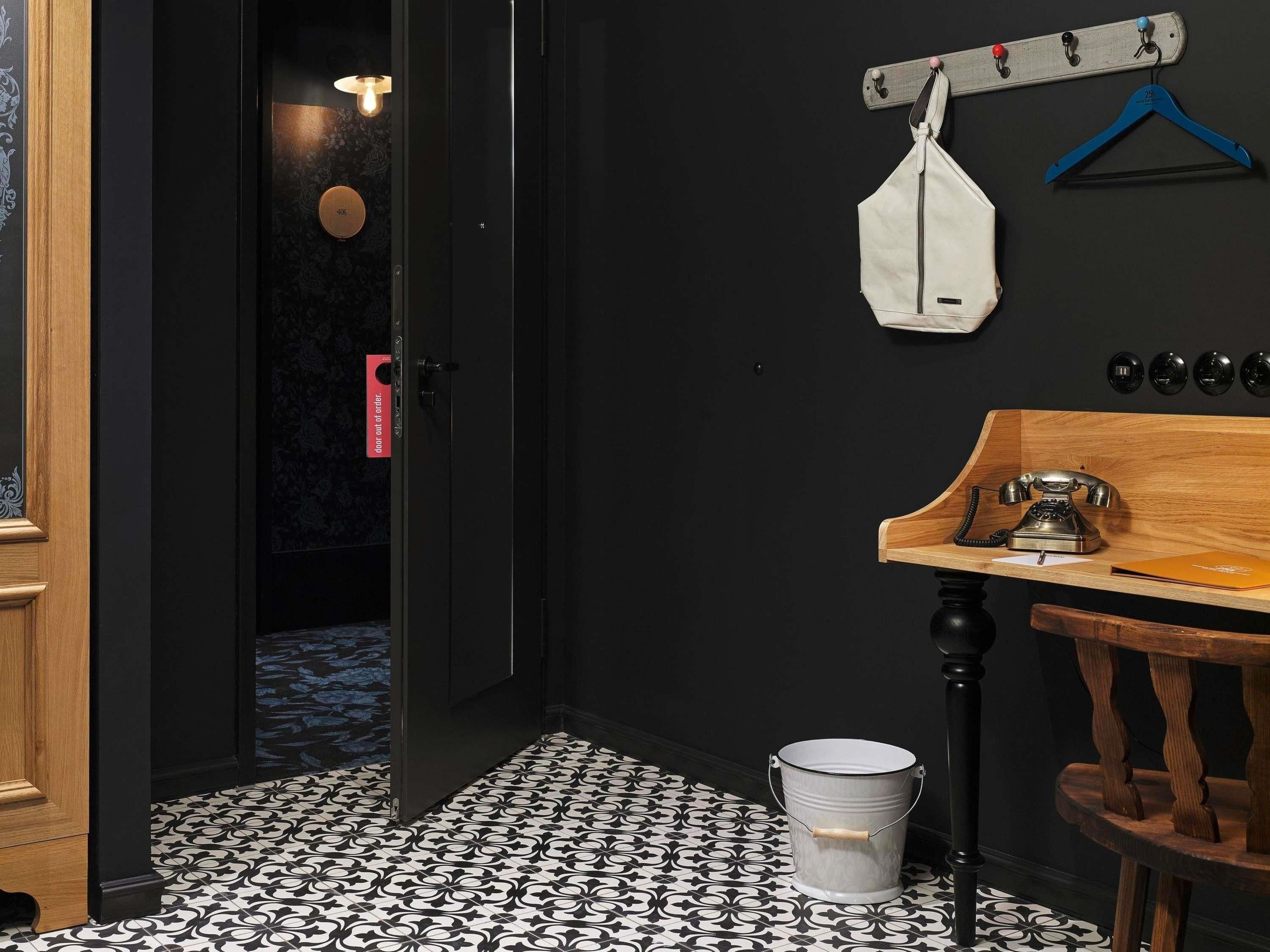 A hotel room with a wooden door, a white bucket, a wooden table with a telephone, and a coat rack with hangers.