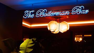 Un letrero de neón que dice "The Botelerman Bar" en una habitación con poca luz y una lámpara ornamentada de gran tamaño.