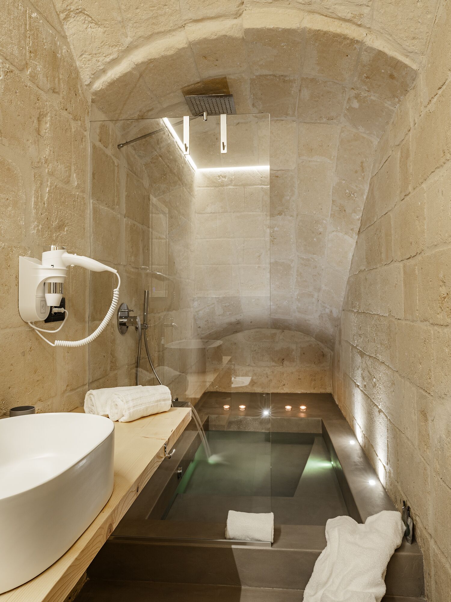 Ein Badezimmer mit Steinwänden, einer Badewanne, einem Waschbecken und einem Föhn.